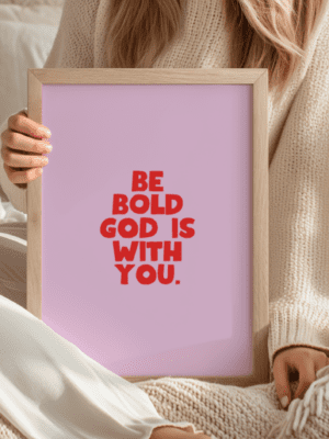 framed poster with the bold red text "BE BOLD GOD IS WITH YOU" centered on a soft pink background.