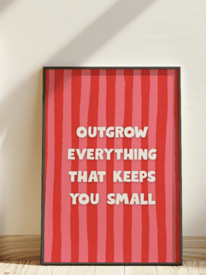 A striking poster with a red and pink striped background. The white text reads: "OUTGROW EVERYTHING THAT KEEPS YOU SMALL." The print is in a black frame, leaning against a white wall.