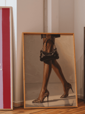 Oil painting style art print of a woman's legs walking in leopard print high heel shoes and carrying a black handbag with gold chains.